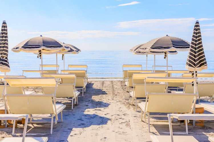 Photo of beautiful beach umbrellas and couches on blue sky and sea background on the beach of Milano Marittima, Cervia, Italy.