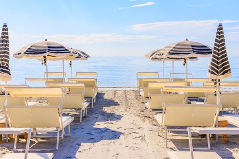 Photo of beautiful beach umbrellas and couches on blue sky and sea background on the beach of Milano Marittima, Cervia, Italy.
