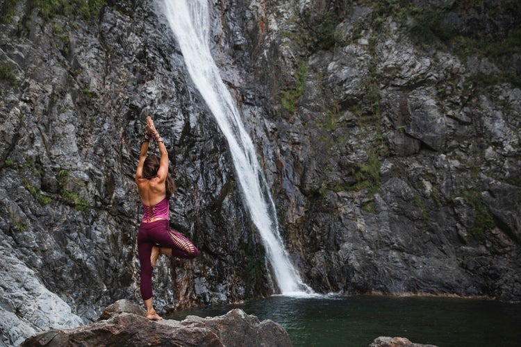 Italy- lecco- woman doing tree yoga pose on a rock near a waterfall