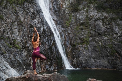 Italy- lecco- woman doing tree yoga pose on a rock near a waterfall