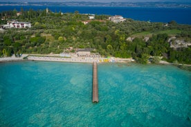 Photo of Old harbour Porto Vecchio with motor boats on turquoise water, green trees and traditional buildings in historical centre of Desenzano del Garda town, Northern Italy.