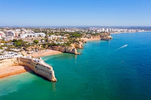 Photo of beautiful aerial view of the sandy beach surrounded by typical white houses in a sunny spring day, Carvoeiro, Lagoa, Algarve, Portugal.