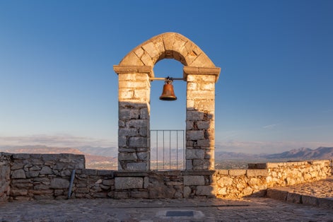 Photo of Bell tower in Palamidi fortress on a hill above vast valley surrounded by mountains, Nafplio, Greece.