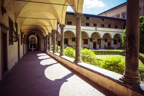 photo of view of Courtyard Basilica di San Lorenzo (Basilica of St Lawrence) with arches, columns and garden on sunny day, Florence, Italy.