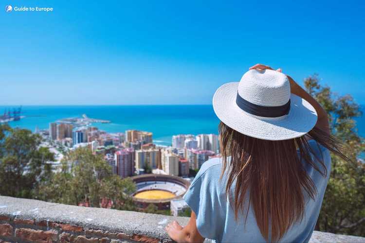 A woman wearing a white hat observes the city of Malaga, taking in the panoramic view of the vibrant city below..png