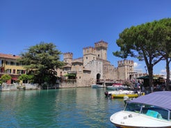 Photo of Old harbour Porto Vecchio with motor boats on turquoise water, green trees and traditional buildings in historical centre of Desenzano del Garda town, Northern Italy.