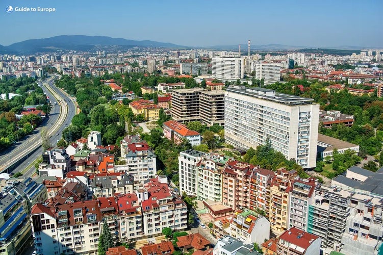 Aerial view of Sofia, Bulgaria, showcasing residential buildings, tree-lined streets, office buildings, and distant mountains under the sky..jpg