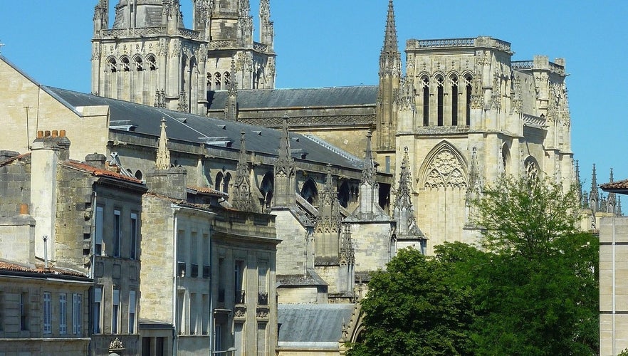 Side view of Saint-André Cathedral in Bordeaux with Gothic spires rising above rooftops and trees under a clear sky..jpg