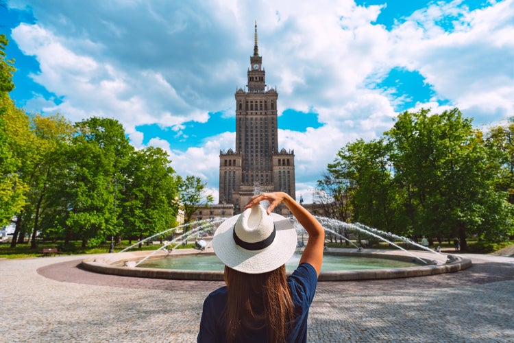 Photo of tourist woman in white sun hat walking in the park near Palace of Culture and Science in Warsaw, Poland.