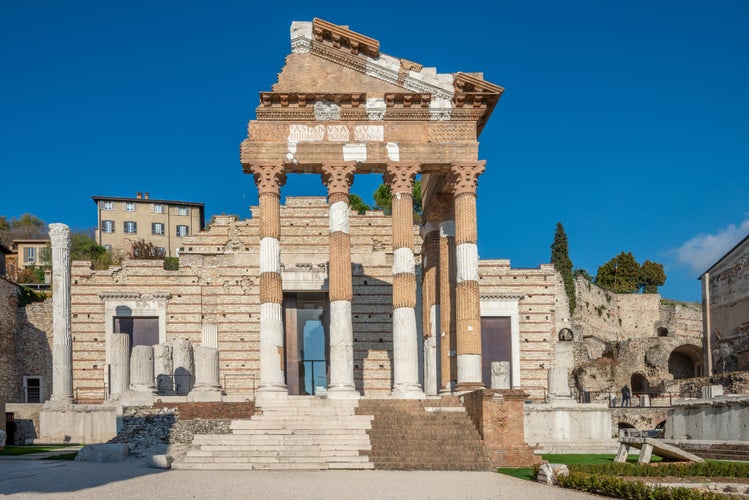 the ancient Roman ruins in Brescia, Italy, showcasing the weathered yet majestic columns of a temple. The detailed carvings and inscriptions on the stone structures reflect the grandeur