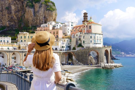 photo of holiday in italy. Back view of young woman with white dress and hat looking the village of atrani on amalfi coast, Italy.