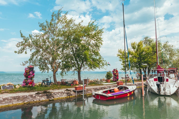 photo of view of View to entrance to Siofok harbor at Balaton lake, Hungary, with crystal clear water of emerald color, green coastline, puffy clouds on sky