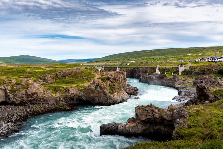 A river from Godafoss Falls, Akureyri, Iceland, surrounded by huge rocks and a concrete bridge