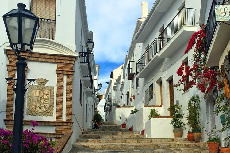 A charming narrow street in Frigiliana with white buildings and blooming flowers offering a delightful and picturesque scene. .png