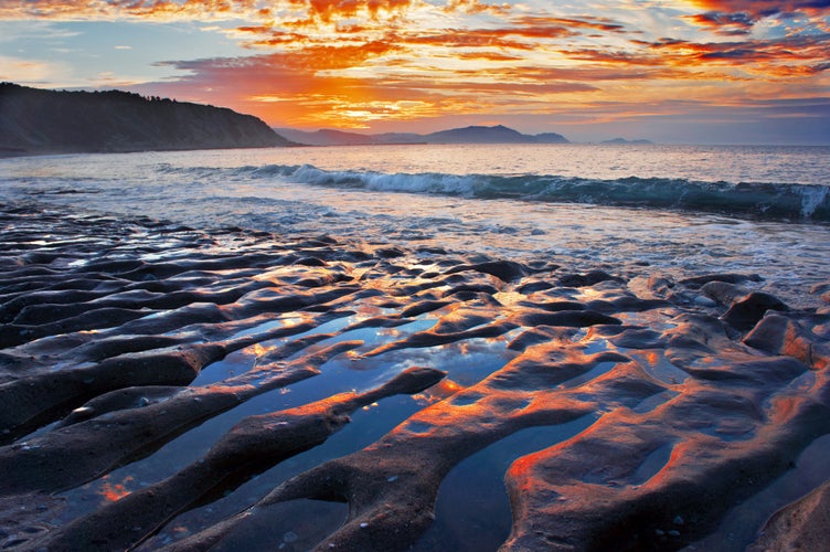 Azkorri beach at sunset with sky reflections on the rocks.