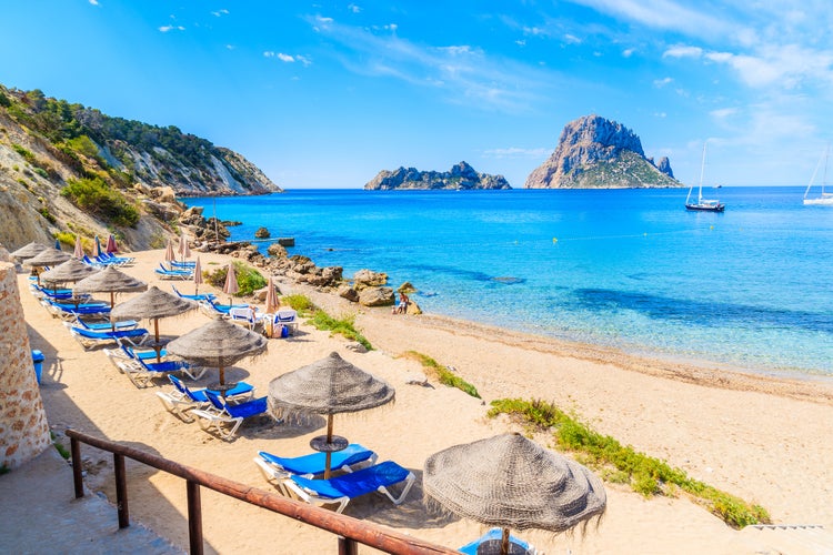 View of Cala d'Hort beach with sunbeds and umbrellas and beautiful azure blue sea water, Ibiza island, Spain