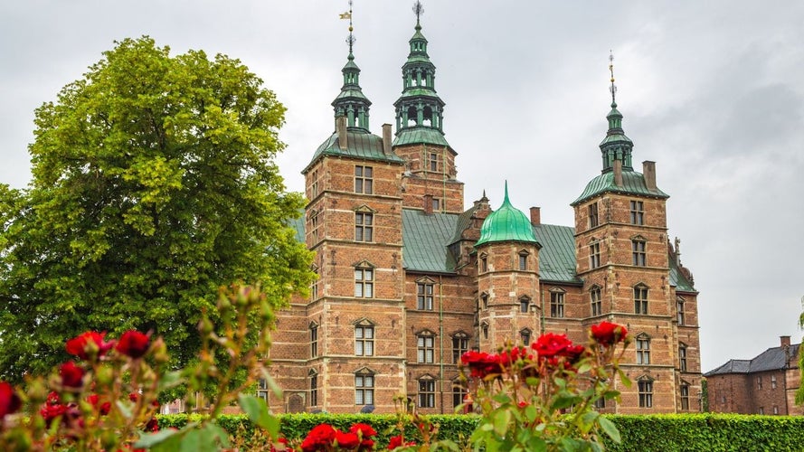 Rosenborg Castle in Copenhagen surrounded by vibrant red flowers and lush green trees on a cloudy day..jpg