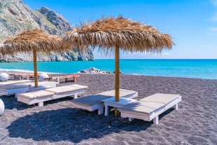 Photo of aerial view of black Perissa beach with beautiful turquoise water, sea waves and straw umbrellas, Greece.