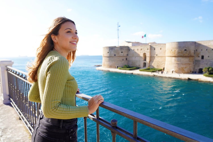 Portrait of smiling relaxed traveller woman looking Taranto city from seafront, Italy.