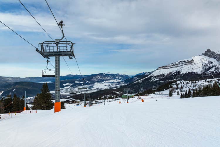 Empty chair lift at french Villard de Lans ski resort surrounded by snowy Vercors mountains.