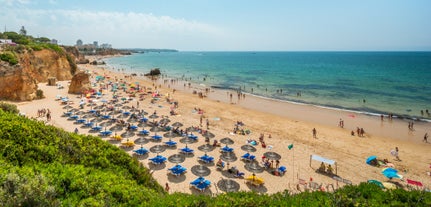 Photo of beautiful aerial view of the sandy beach surrounded by typical white houses in a sunny spring day, Carvoeiro, Lagoa, Algarve, Portugal.