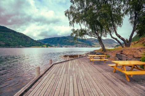 photo of view of View of the Sognefjord on a cloudy day. Wooden embankment with rest place near the fjord. Kjornes Camping, Sogndal, Norway