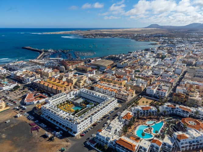 Aerial view Corralejo town, harbour, black rocks, blue water, Lobos and Lanzarote islands, Fuerteventura, Canary islands, Spain, winter sun vacation