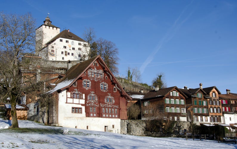 Photo of Old medieval city center Buchs of Werdenberg in a region St. Gallen in Switzerland with wooden and stone houses and the medieval castle on the hill on a cloudy day in winter.