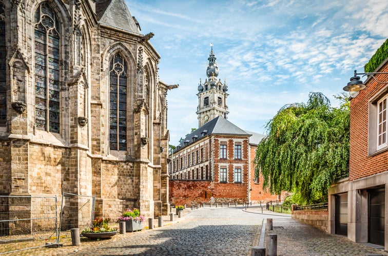 Cobbled street with church and belfry tower in Walloon city center of Mons, Hainaut, Belgium.