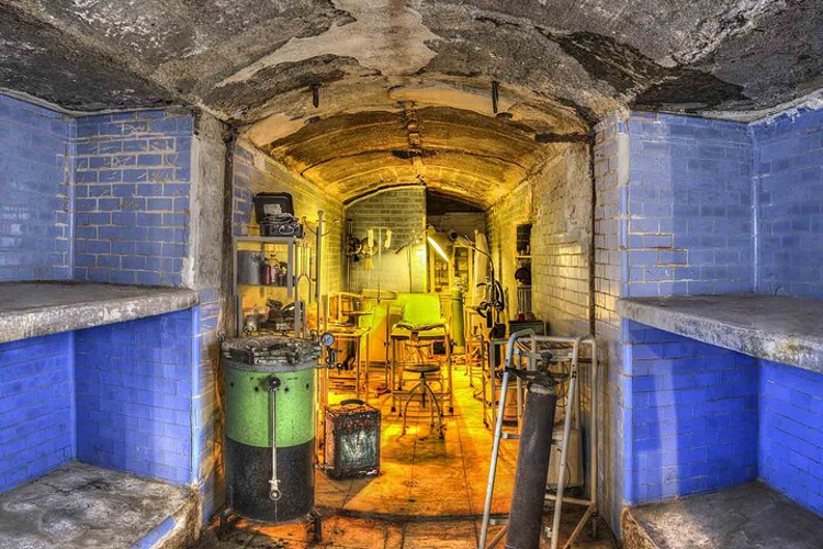 An underground Spanish Civil War shelter in Almeria with blue-tiled walls, aged ceilings, and vintage medical equipment..png