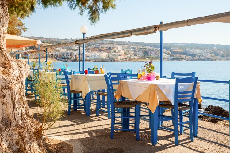 Photo of greek cafe terrace in Heraklion, Crete overlooking the sea with typical wooden chairs.