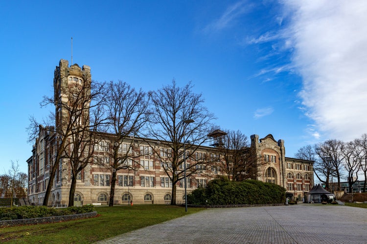 photo of view of Empty esplanade with old main building of former Waterschei mine in background against blue sky, bare trees, Thor Park - Hoge Kempen National Park, sunny autumn day in Genk, Belgium