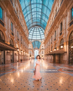 photo of Milan, Italy - August 12, 2018: An isolated girl in the middle of the galleria vittorio emanuele II in Milan with a pink dress and a straw hat.