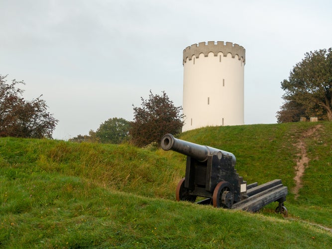 photo of view of Old white water tower on rampart in city Fredericia, Denmark.Old bronze cannon on rampart in city Fredericia, Denmark.