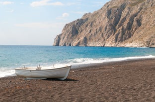 Photo of aerial view of black Perissa beach with beautiful turquoise water, sea waves and straw umbrellas, Greece.