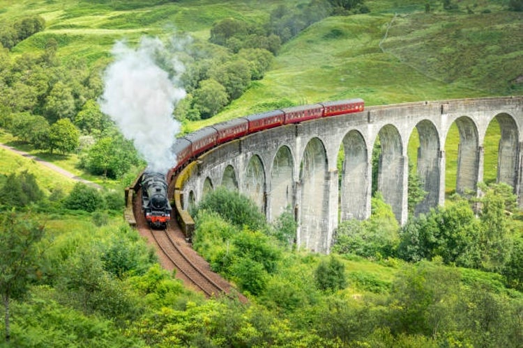 The Jacobite Steam Train crossing the iconic Glenfinnan Viaduct in Scotland, with its billowing smoke trailing behind.jpg