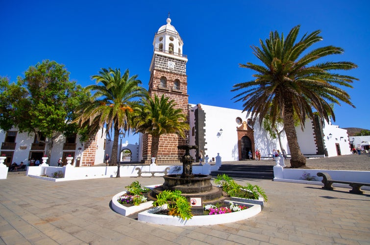 Costa Teguise village square with a church and a brick tower surrounded by streetlights Palm trees and little White Houses on a Sunny summer day. Touristic resources of Lanzarote Canary islands.