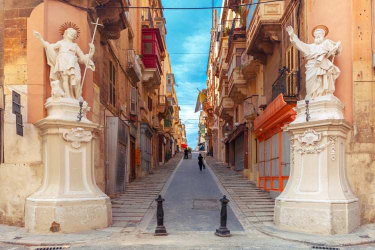 Photo of the traditional Maltese street stairs with corners of houses, decorated with statues of saints St. John and St. Paul and building with colorful balconies in Valletta, Capital city of Malta.