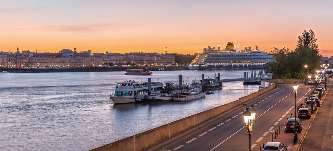 Cruise ship and boats docked along the Garonne River in Bordeaux at sunset with city lights and pastel skies..jpg