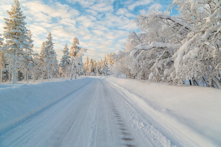 Winter road with snowy trees hanging over it, blue sky with clouds, nice warm light, Gällivare, Swedish Lapland, Sweden