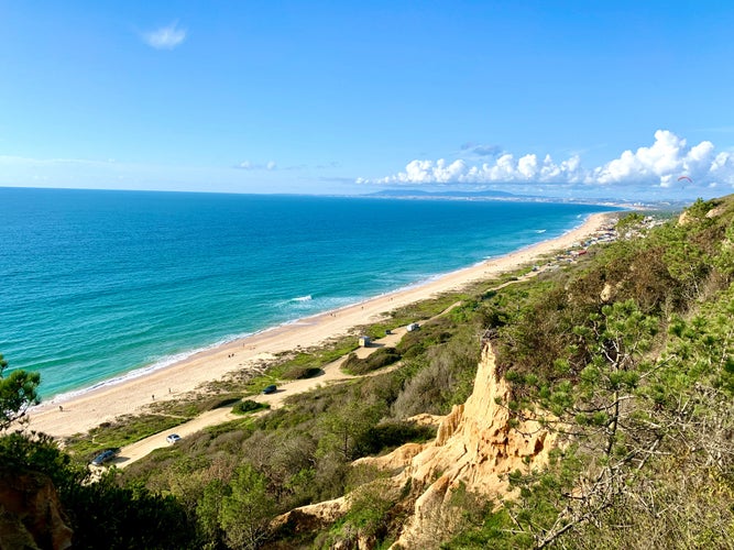 Photo of Beautiful landscape with green pine tree, turquoise blue water ocean, and beautiful blue sky in Fonte da Telha, Costa da Caparica, Portugal.