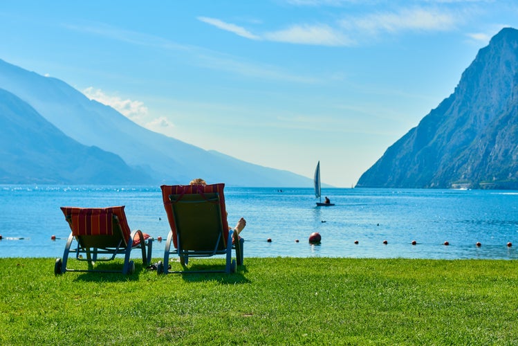 People sitting at the beach on the lounge chair and admiring Lake Garda in the summer time,View of the beautiful Lake Garda surrounded by mountains