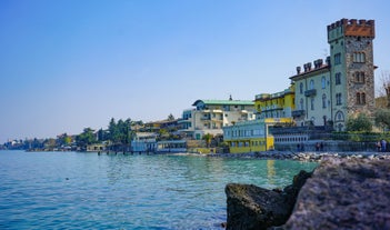 Photo of Old harbour Porto Vecchio with motor boats on turquoise water, green trees and traditional buildings in historical centre of Desenzano del Garda town, Northern Italy.