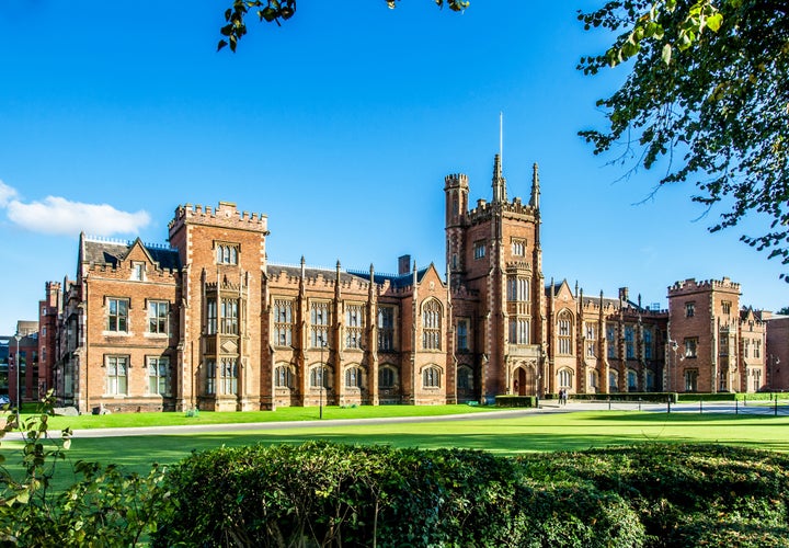 Photo of the Queen's University of Belfast with a grass lawn, tree branches and a hedge in sunset light.