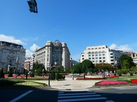 Photo of aerial view of Bilbao, Spain city downtown with a Nevion River, Zubizuri Bridge and promenade. Mountain at the background, with clear blue sky.