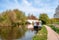 Photo of a narrow boat moored at the river Gade, Grand Union Canal. The Grove Bridge aka Grove Ornamental Bridge No 164 is in the background, Cassiobury Park, Watford, England.