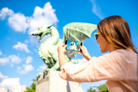 Young female traveler photographing with smart phone Dragon statue on the bridge in Ljubljana city. Dragon statue is one of the most famous symbols of the capital of Slovenia