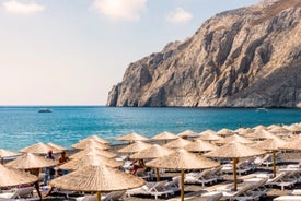 Photo of aerial view of black Perissa beach with beautiful turquoise water, sea waves and straw umbrellas, Greece.