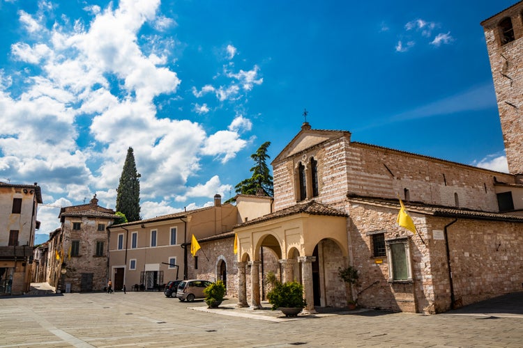 Photo of the Basilica of Santa Maria Infraportas, an ancient medieval church, with its tower. The yellow flag of one of the districts. In Foligno, Perugia, Umbria, Italy.