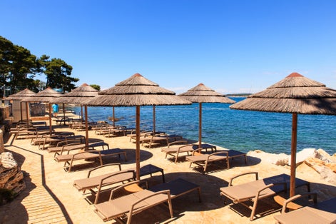 Photo of Beach and resort with beach chairs and umbrellas in morning light on the beach of a Croatian seaside holiday resort in Porec.